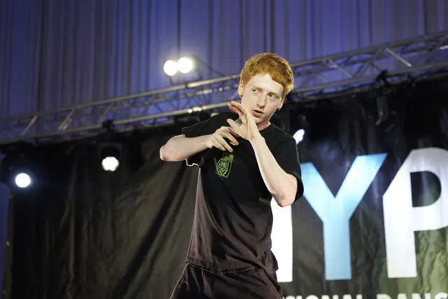 Tanečník s mikrofónom na pódiu pred bannerom HYPE