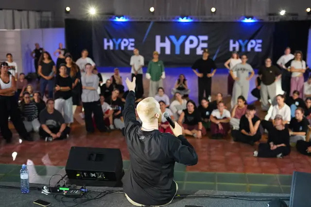 A dancer seen from behind facing a seated crowd of students, HYPE banner and speakers